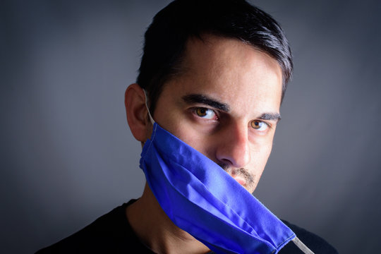 Man Taking Off Mask With Protective Mask On Face Against Coronavirus. COVID-19 Pandemic Coronavirus. Man Portrait With Homemade Mask. Young Man With Homemade Protective Mask, With Black Tshirt.