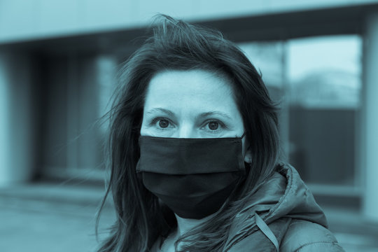 Tinted blue portrait of a woman with a black medical mask on the background of a business building, the concept of a pandemic threat.