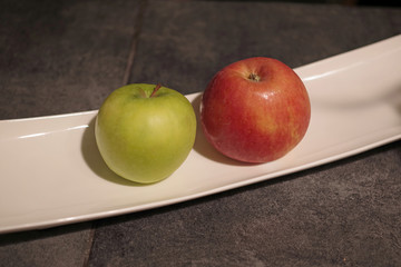Close-up view of a green and a red apple on a white rectangular long porcelain plate