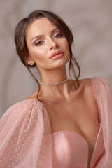 Elegant interior portrait of young beautiful brunette woman with perfect makeup and hairstyle. Closeup face portrait in pink evening dress with decollete