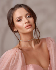 Elegant interior portrait of young beautiful brunette woman with perfect makeup and hairstyle. Closeup face portrait in pink evening dress with decollete