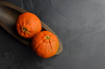 Two fresh mandarin citrus fruits in wooden plate on black background. Winter time fruits. Top view,...