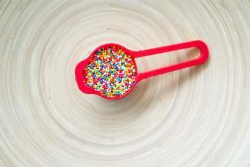 Colourful Sugar sprinkles in measuring cups. Decoration for cake and ice-cream and cookies. Top view, Flat lay on wooden background.