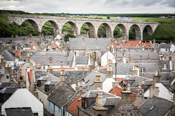 Old croft houses in Cullen, fishing village on Moray Firth, Scotland. Cullen Viaduct in the background, old roofs and chimneys - obrazy, fototapety, plakaty