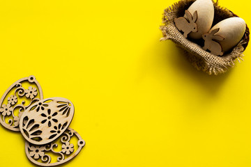 Flatlay with different wooden eggs on a yellow paper background with copy space