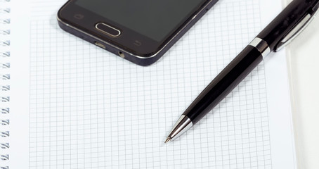 Pen, smartphone and notebook on a white background close-up