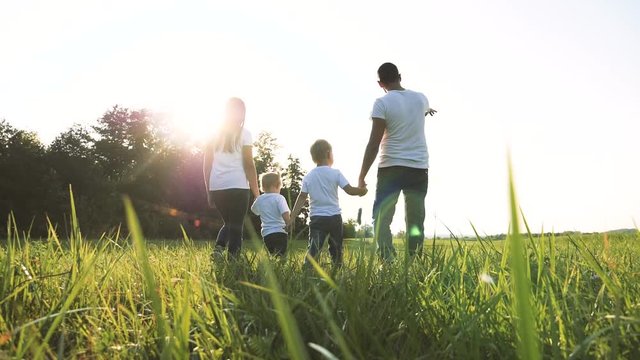 happy family teamwork daddy mother, little brother and sister walk in the park nature holding hands slow motion video concept. father mom, kids boy and girl daughter and son hold hands go on green