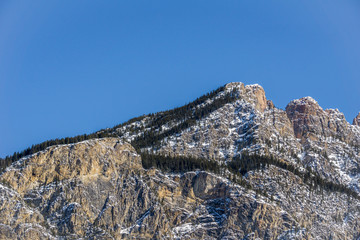 close-up view of the mountain peak with trees and snow on it sunny spring day.