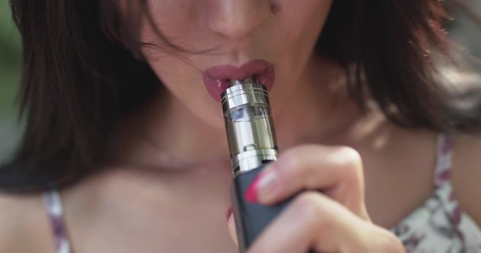 Macro view of female seductive smoking e-cigarette and exhales at camera