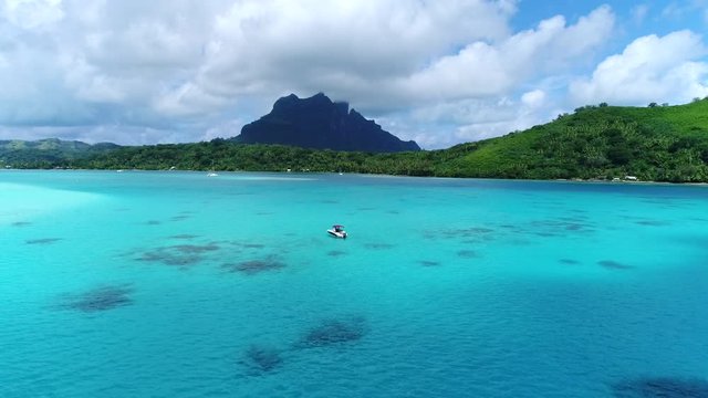 Beautiful drone shot of a speedboat in tropical island vacation hotspot Bora Bora, French Polynesia. Boat floating in the blue turquoise south pacific water and mountain peaks dot the landscape