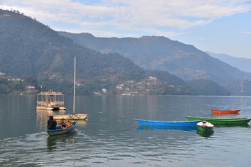 ネパールの山岳都市のポカラ　美しいペワ湖と山林と青空　ボートで荷物を運ぶネパール人男性