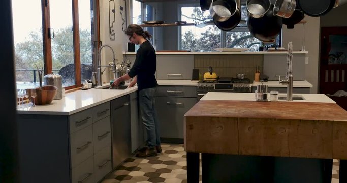 Dolly shot of a man washing dishes in a sink in a modern kitchen