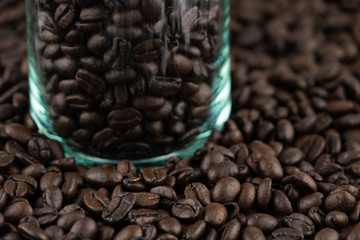Roasted coffee beans in the clear glass jar on coffee beans background
