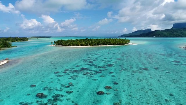 Amazing drone shot of secret tropical island in the turquoise blue lagoon of paradise vacation destination Bora Bora, French Polynesia. Flying away from the island over the waters of the south pacific