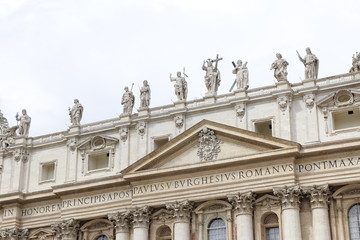 Fototapeta na wymiar Statues of Christ and the Apostles and Oltramontano Clock on top of the facade of St Peter's Basilica with blue sky and clouds in Vatican City