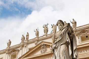 Statue of St. Paul with sword in front of St Peter's Basilica with blue sky and clouds in Vatican City, Rome, Italy