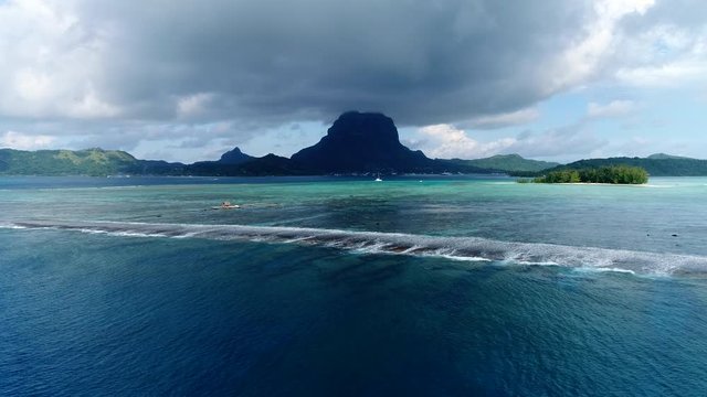 Dramatic drone shot of the tropical lagoon reef break of paradise island  Bora Bora. Flying towards moody rain clouds and moutain peaks over the blue water of the South Pacific 