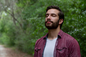 young man with brown hair and beard wearing red button down breathes in a breath of fresh air...