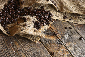 Obraz na płótnie Canvas A close up image of dark roasted coffee beans and burlap sack on an old wooden table. 