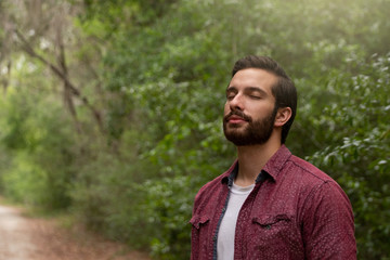 young man with brown hair and beard wearing red button down breathes in a breath of fresh air...