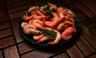 fresh large shrimps on a plate with greens on a background of wooden tiles