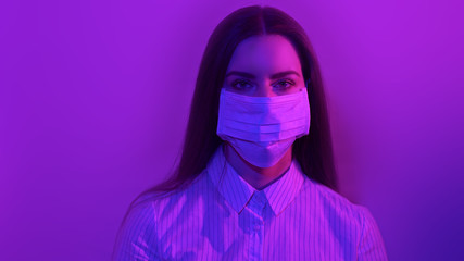 Portrait of girl that wearing protective surgical mask on face in neon lights. Fashion luxury shot, epidemic disease covid-19 virus, patient in mask isolated in dark background