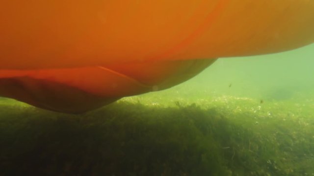 Under water footage of paddles moving through a river. A raft is seen in view with water bubbling to the top of the water.