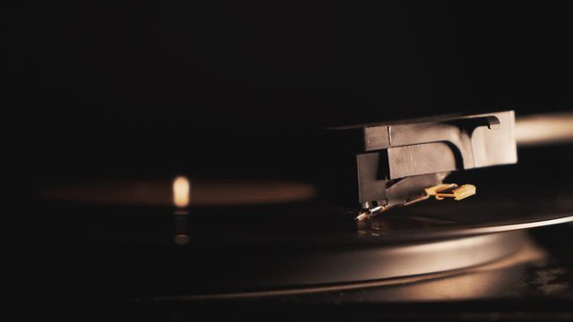 4K Cinemagraph vinyl record spinning close-up turning starting on a dark background with warm colorful light. Close up of turntable tonearm playing. Retro-styled, old school