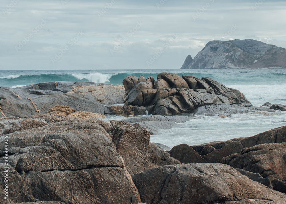 Wall mural dramatic scenery with rough water smashing rocks with an isolated island in the background. this tak