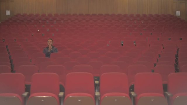 A tall white guy is in an empty theatre. He is the only one watching the show and the rest of chairs are empty. He stands up and starts to clap because he enjoys what he sees on stage.