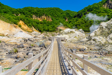 Fototapeta na wymiar View of wooden pathway for sightseeing in Jigokudani valley or hell valley and blue sky background in summer. Natural Landscape and active volcano in Noboribetsu, Hokkaido, North of Japan.
