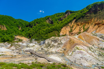 Fototapeta na wymiar Scenery of Jigokudani valley or hell valley and blue sky background in summer. Natural Landscape and active volcano in Noboribetsu, Hokkaido, North of Japan.