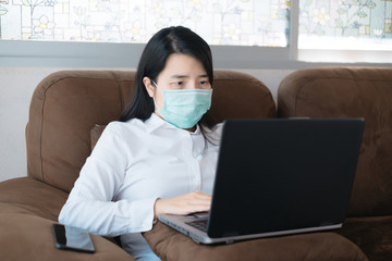 Asian women use laptop in working at home and wearing mask for protect COVID-19