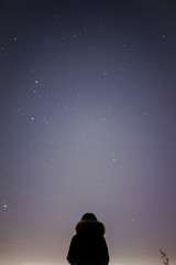 Fototapeta na wymiar A woman with winter-jacket looks the stars over the dark sky.