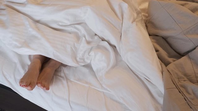feet dance and hide under blanket,Close-up of feet of young woman out from under covers in bedroom. Bare feet