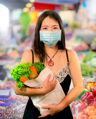 groceries shooping during covid-19 virus quarantine - young beautiful and positive Asian Chinese woman in mask carrying vegetables bag stock up during coronavirus lockdown