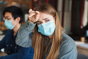 Image of unhappy woman in protective mask touching her forehead