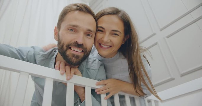 Happy young parents watching at sleeping baby in crib