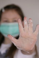 Fototapeta premium Clean hands . Hand washing.Coronavirus epidemic.Girl child in a medical protective mask shows hands in soap foam close-up. Hygiene and health concept.Precautions for viral diseases.