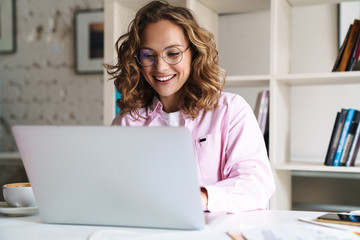 Photo of joyful woman wearing eyeglasses smiling and using laptop