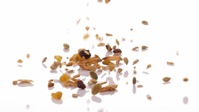 Slow motion speed close up scene of granola dropping on floor on white background, muesli texture, pattern of seed scattered falling and bounce on ground, cereal grain for good health, food industrial