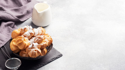 Profiteroles with custard and powdered sugar on a plate. Concrete grey table. Copy space.