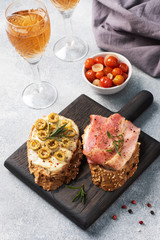 Wholegrain bread sandwiches with cream cheese, bacon and olives on a wooden cutting Board. A glass of white wine. Gray concrete background.