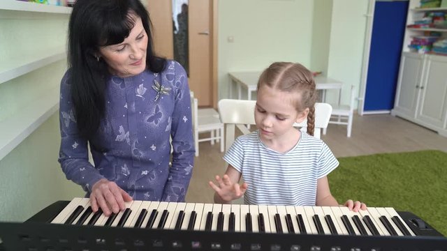 a woman teaches little girl to play on synthesizer