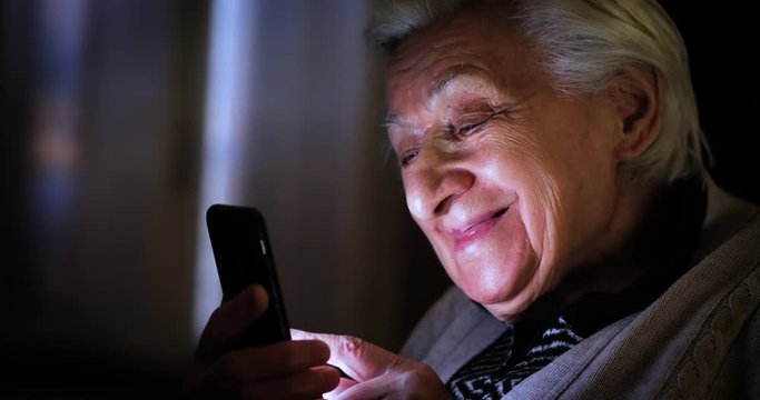 Authentic shot of a happy modern grandmother is using a smartphone for navigate in internet, send messages and make calls. Concept of technology, modern generation,family, connection, authenticity