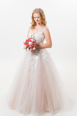 Fototapeta premium Portrait of romantic young bride in white lace wedding dress with fantasy makeup and wavy blonde hair with wedding bouquet in her hands getting ready in bride's morning. Fine art wedding.