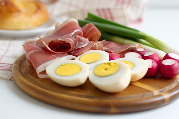 Closeup of boiled eggs, ham, radish and spring onion on wooden cutting board