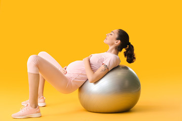 Young pregnant woman doing exercises with fitball on color background