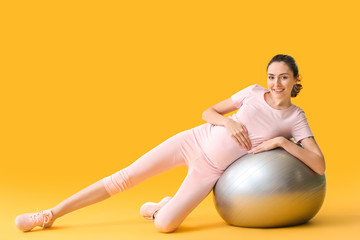 Fototapeta na wymiar Young pregnant woman doing exercises with fitball on color background