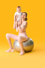 Young sporty mother and her baby doing exercises with fitball on color background